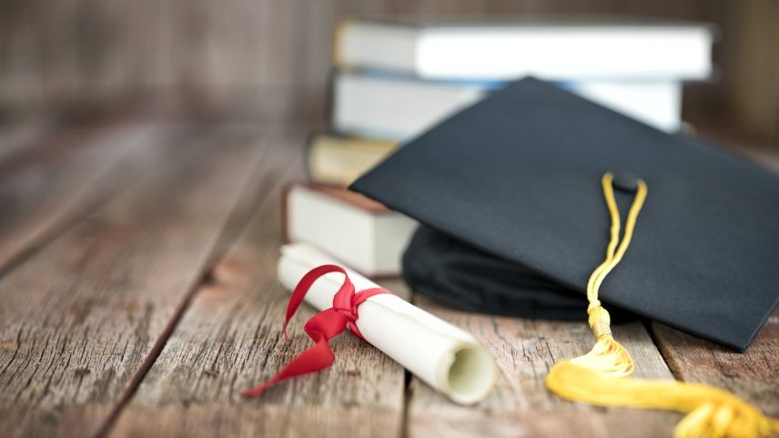 Capelo de formatura e diploma com uma pilha de livros sobre um fundo de madeira (Foto: Liliboas/Getty Images)