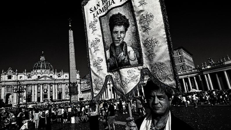 Pessoa segura um banner de Carlo Acutis na Praça de São Pedro, no Vaticano (Foto: Reprodução)