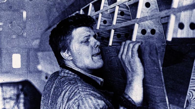 Homem em uma exposição de arte, posando ao lado de uma obra (Foto: Reprodução)