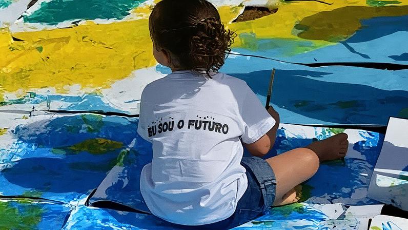 Criança sentada no chão com as cores da bandeira brasileira e com uma camiseta branca escrita Eu Sou o Futuro na cor azul • Wilson Dias/Agência Brasil