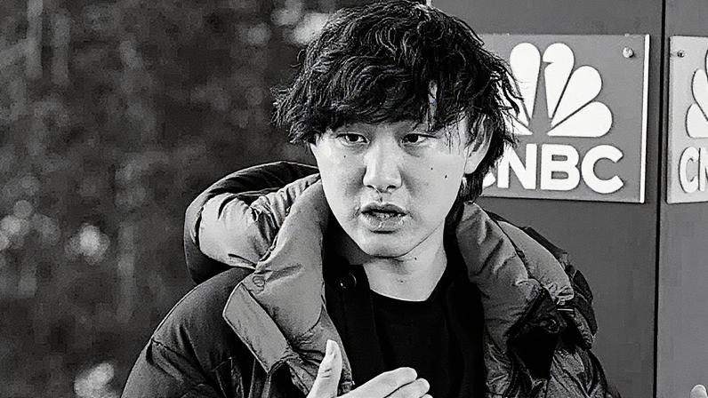 Homem de terno fala ao microfone durante apresentação em um palco com gráfico ao fundo (Foto: Reprodução)