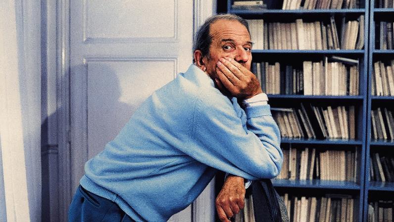 Homem com terno em pé, falando ao microfone, com um grande telão ao fundo exibindo um gráfico azul em ascensão (Foto: Reprodução)